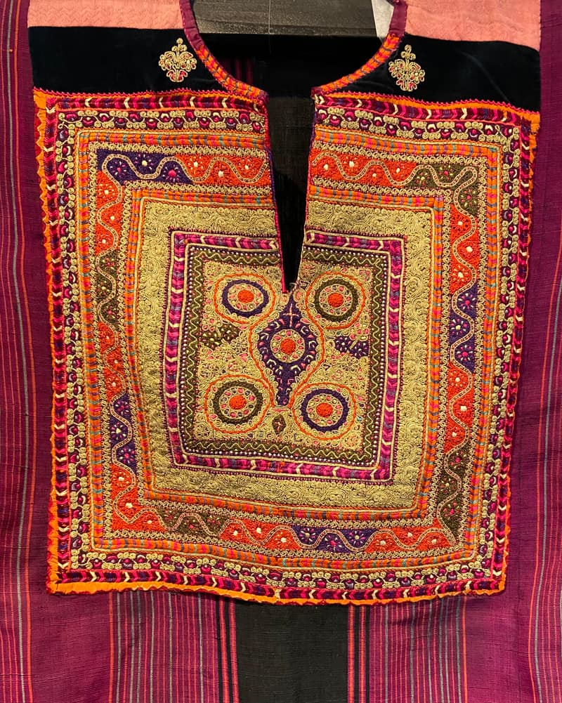 The embroidered chest panel of a Bethlehem dress, laid flat: concentric rectangular borders in orange, magenta, violet and gold cord surrounding four circular rosettes, set on black velvet above a striped purple ground.